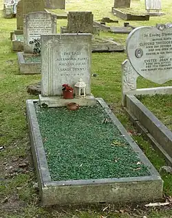 A grave covered with emerald-like gravel, with a granite headstone, surrounded by other graves