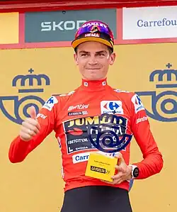 Kuss wearing a red cycling jersey and holding a trophy.