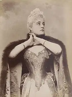 Black and white photograph of a woman in luxurious eighteenth-century garb, gazing pleadingly above her