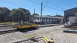 Workshop yard showing shunting tractor in background, stabled carriages, maintenance trolley and electric fence