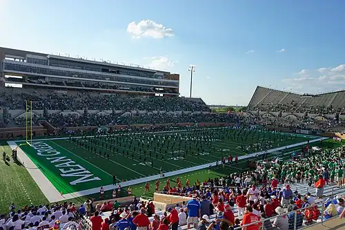 A marching band performs on the field of a football stadium.