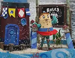 A costumed mascot of Mrs. Puff waving to an audience while standing on a float