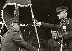 Commander of the Lithuanian Army Stasys Raštikis holds the Lithuanian Army flag with Vytis on obverse side, while a Lithuanian soldier swears his loyalty by kneeling in front of it
