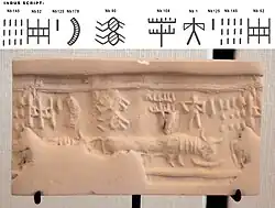 A modern impression of an Indus cylinder seal discovered in Susa, in strata dated to 2600–1700 BCE. Elongated buffalo with line of standard Indus script signs. Tell of the Susa acropolis. Louvre Museum, reference Sb 2425.[68][69] Indus script numbering convention per Asko Parpola.[70][71]