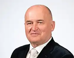 a photo of this person. they are bald and are wearing a business suit with a white tie