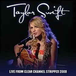 Swift seated with a guitar in front of a microphone