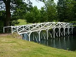 A colour photograph of a wooden bridge painted white crossing a narrow water-filled channel