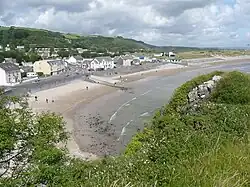 Small sandy cove and beach with slipway and buildings taken from an elevated camera position on a sunny day