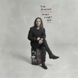 A man with long hair sits on a suitcase, with the words "Apart Together" written above him