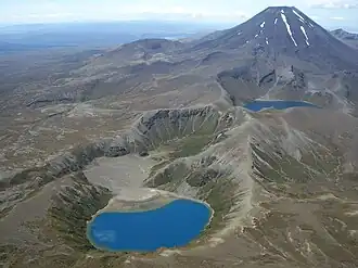 A volcanic landscape with two small blue crater lakes in the centre and a triangular peak in the background