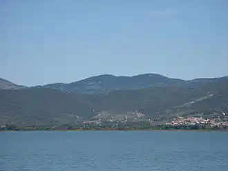 A colour photograph from the middle of a lake of the lake shore with low hills beyond