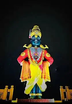 A stone icon of an arms-akimbo man standing on a brick and wearing a dhoti, angarkha (shirt), uparna (cloth across the chest) and a crown.