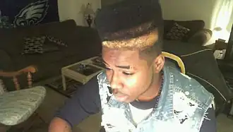 American teenager with hi-top fade and distressed acid wash denim vest, 2010, showing early 2010s retro revival trends.