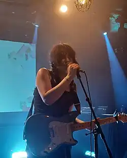 A woman with black pigtails singing into a microphone and holding an electric guitar