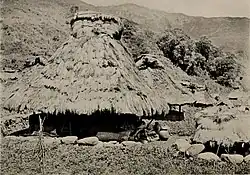 A round, thatched building, its roof overhanging the single main room. Other, similar houses can be seen around it.