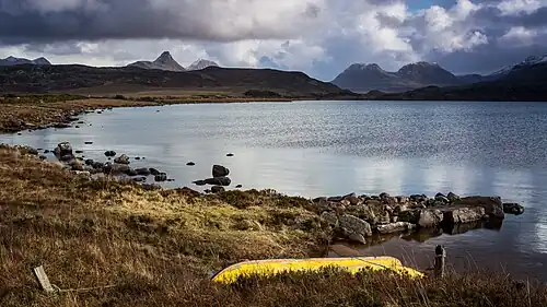 Upturned boat on Loch Osgaig. Looking at the right is the twin peaks of Sgorr Tuath and Sgorr Deas. In the middle is the foreground peak of Stac Pollaidh to the left and Cùl Beag behind. To the left is the peak of Cùl Mòr