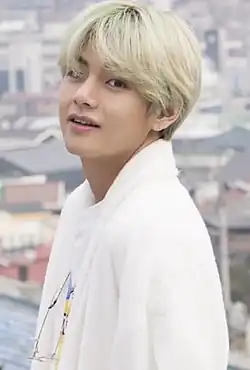 V, in all white, smiles and faces left