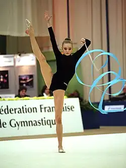 Stadnik stands in a split and twirls the ribbon