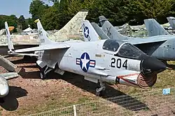 Left quarter view of an F-8E(FN) Crusader. The aircraft is painted in US Navy markings, with a large American roundel and the number 204 prominently on its nose. The aircraft's wings are folded.