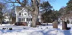 House with carriage barn in background. Large deciduous tree in front of house; square brick piers in foreground