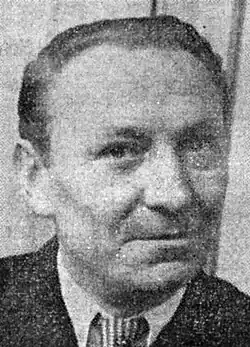 A black-and-white image of a man smirking behind the camera.