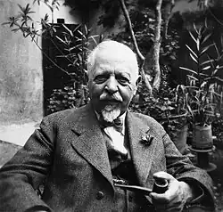 Black and white photograph of Alexander Zahlbruckner holding a pipe, with plants behind him