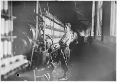 A black and white photograph of a child laborer working in a textile mill